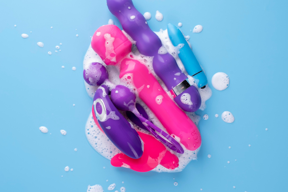 A big variety of sex toys covered in lather on a blue background.