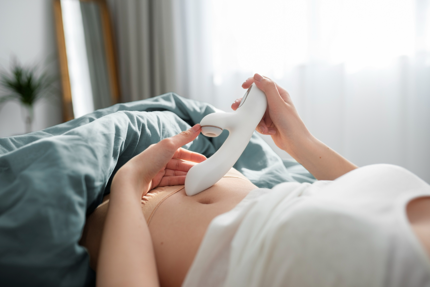 A female in the bed with a white rabbit vibrator in her hands.