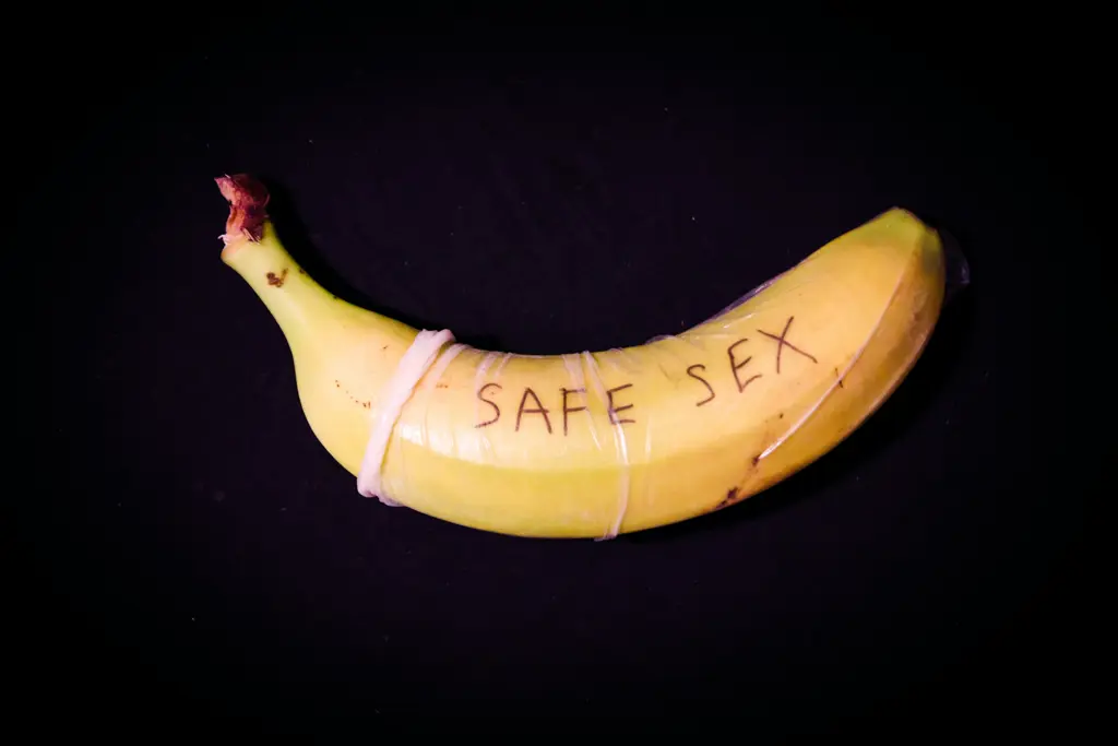 Banane, die mit einem Kondom bedeckt ist und auf dem der Ausdruck "Safe Sex" geschrieben steht.